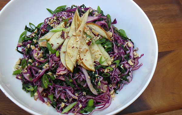 sliced pears atop red cabbage with green onions in a white bowl