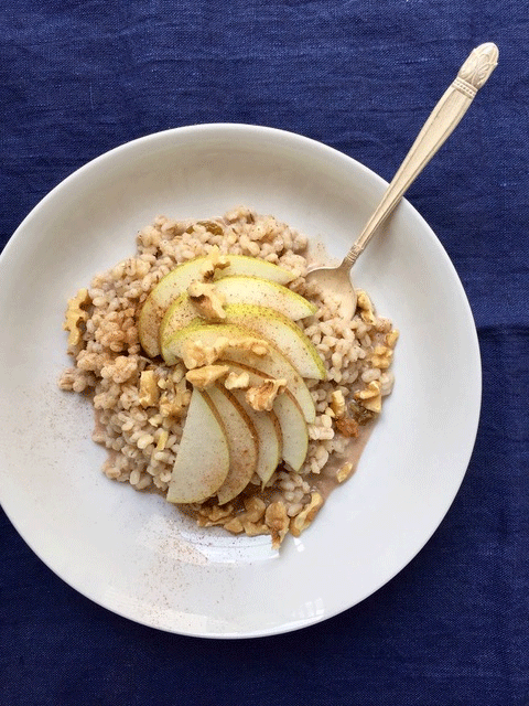 A white bowl of barley topped with pears and walnuts on a blue tablecoth