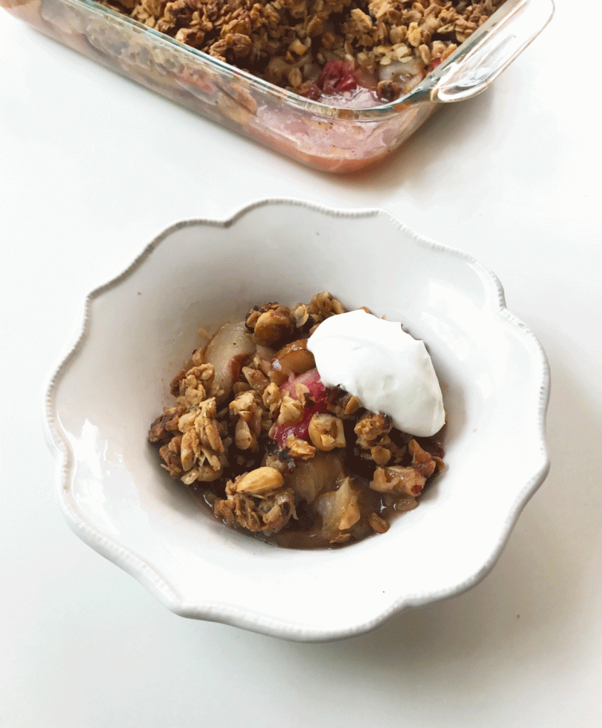 Baked pear and rhubarb crisp in a white bowl with a dollop of Greek yogurt