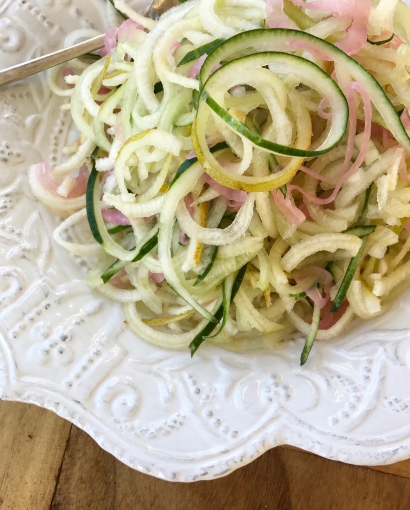 spiralized pears and cucumbers in a white bowl on a wood grain background