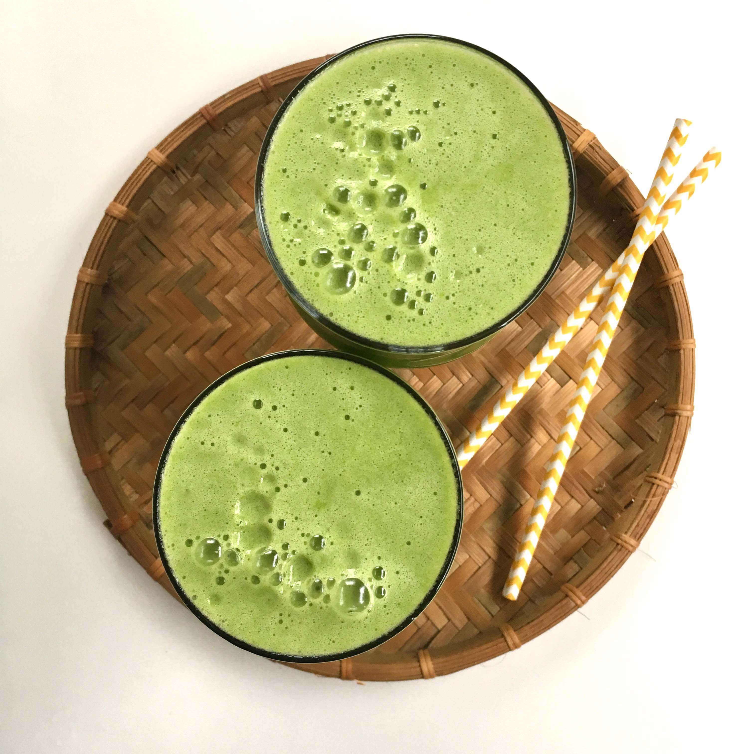 Green, frothy fresh pear juice in glasses on a bamboo mat with straws